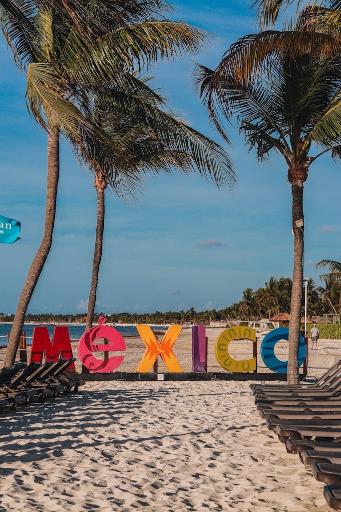 Colorful Mexico sign on a sandy beach with palm trees, perfect for travel enthusiasts.